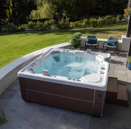 Hot Spring Vanguard Hot tub on a patio with greenery and outdoor furniture in the background