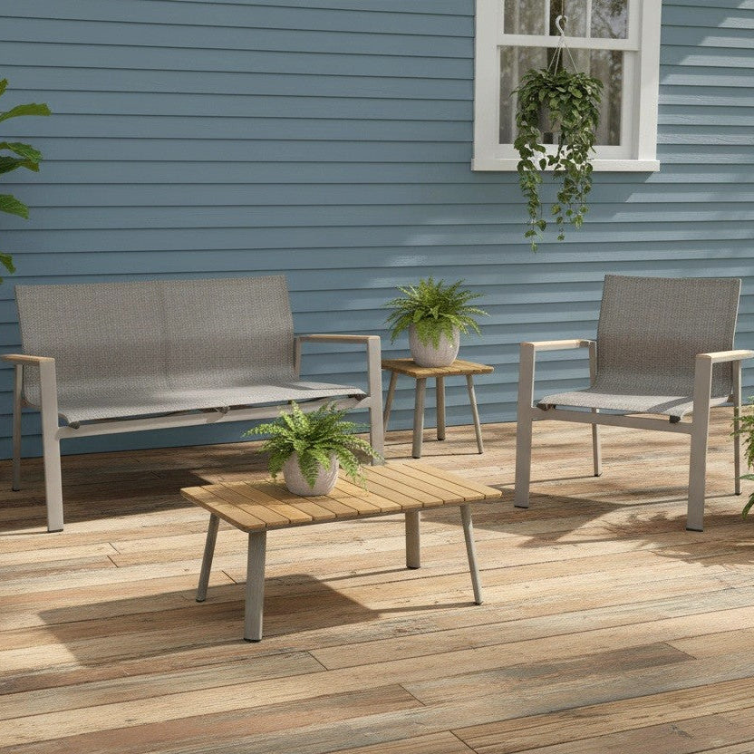 This is a lifestyle image showing this patio furniture set on a weathered wood back porch up against a blue house. There are small potted plants on the coffee table and the end table.