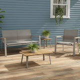 This is a lifestyle image showing this patio furniture set on a weathered wood back porch up against a blue house. There are small potted plants on the coffee table and the end table.