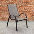 This is a lifestyle image showing this specific sling chair on a stone patio in front of an orange-ish colored brick wall.