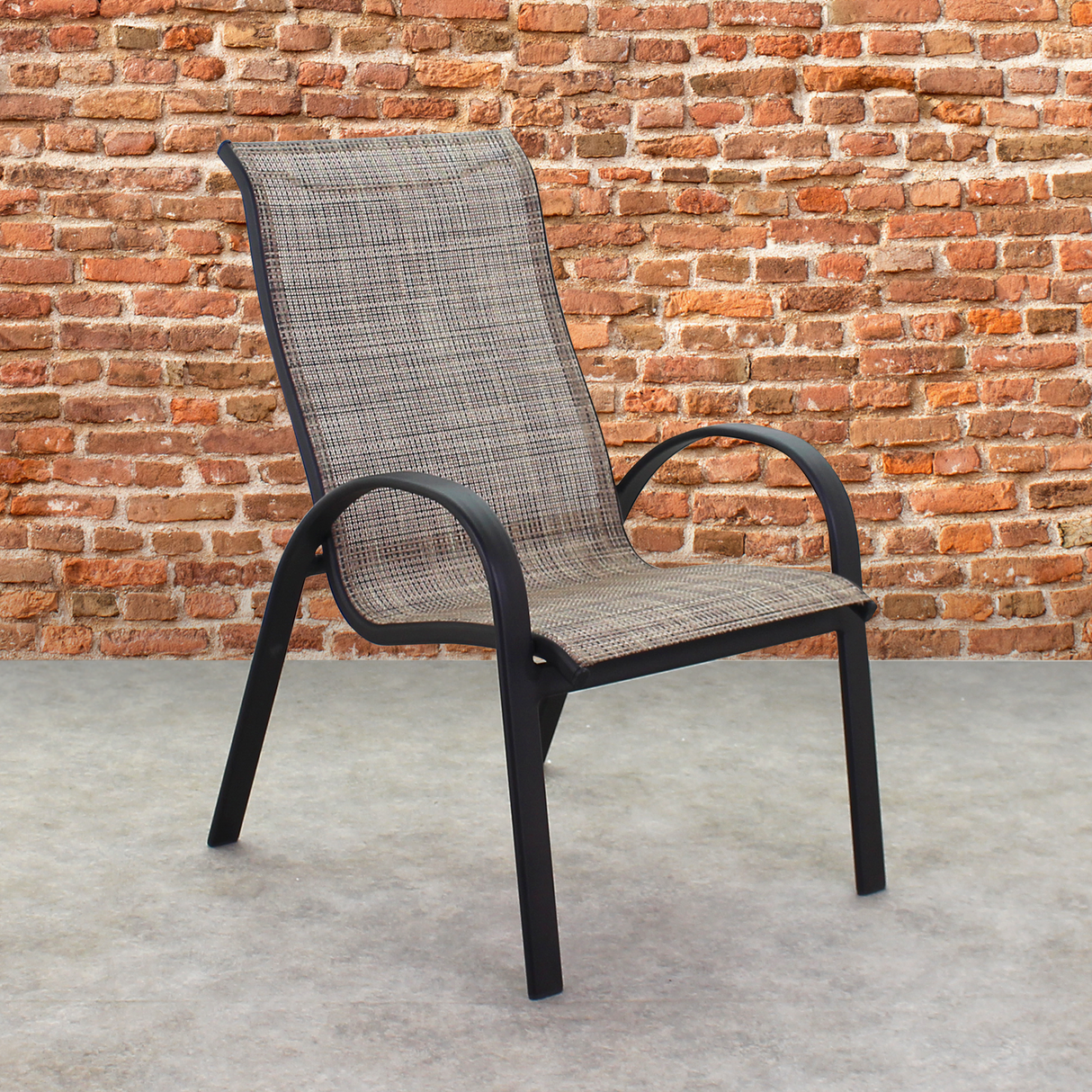 This is a lifestyle image showing this specific sling chair on a stone patio in front of an orange-ish colored brick wall.