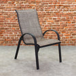 This is a lifestyle image showing this specific sling chair on a stone patio in front of an orange-ish colored brick wall.