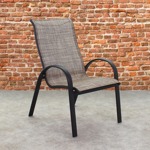 This is a lifestyle image showing this specific sling chair on a stone patio in front of an orange-ish colored brick wall.