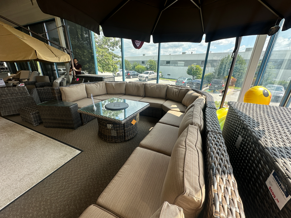 Clearance outdoor sectional patio furniture set with a table, seating and umbrella near a large window with a view of trees and sky.