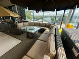Clearance outdoor sectional patio furniture set with a table, seating and umbrella near a large window with a view of trees and sky.
