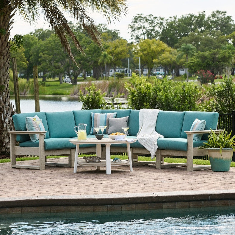 This is a lifestyle image showing the deep seating sectional set on a brick patio next to an in-ground pool. The frames are birch and the cushions are cast breeze.