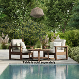 This is a lifestyle image showing two deep seating chairs around a small, round coffee table. The frames are antique mahogany and the cushions are canvas. They're on a stone patio next to an in-ground pool. The image reads "table is sold separately."