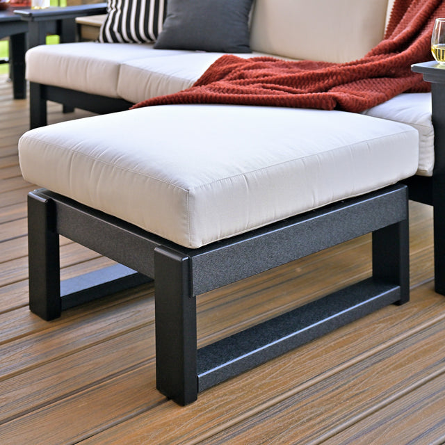 This is a lifestyle image showing the ottoman with black frames and a canvas colored cushion.