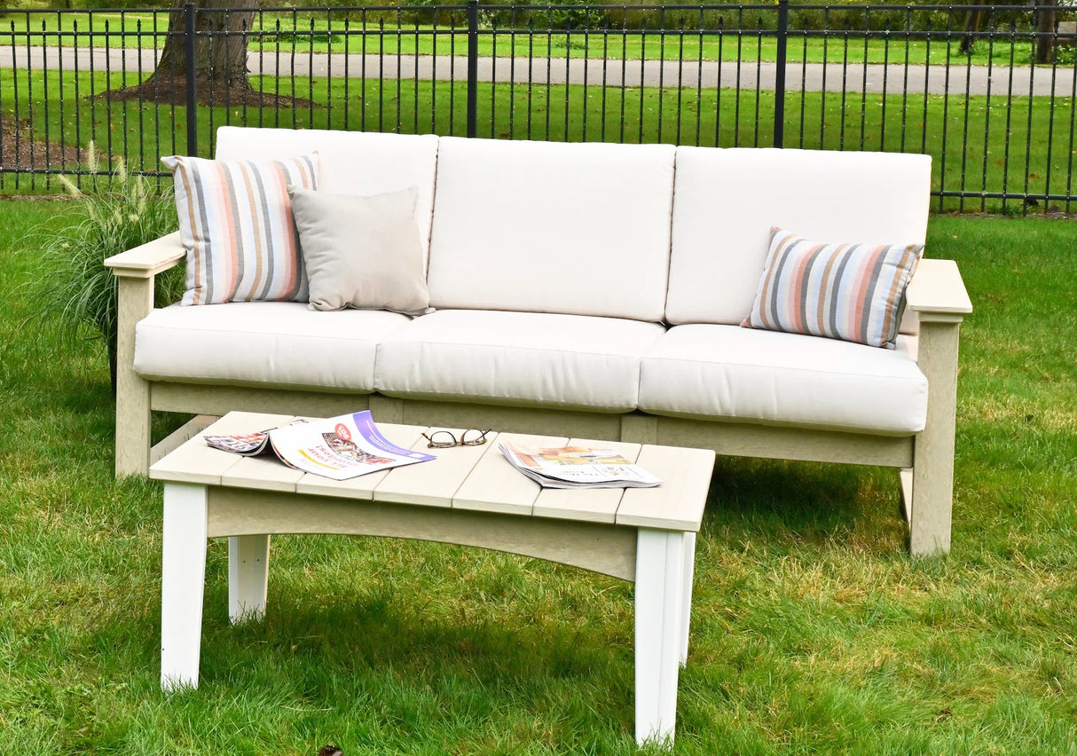 This is a lifestyle image showing this deep seating sofa in a grassy backyard. The frames of the sofa are birch and the cushions are canvas.