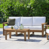 This is a lifestyle image showing the deep seating sofa on an outdoor carpet on a stone patio in a grassy backyard on a sunny day. The frames are antique mahogany and the cushions are canvas.