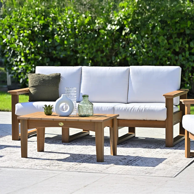 This is a lifestyle image showing the deep seating sofa on an outdoor carpet on a stone patio in a grassy backyard on a sunny day. The frames are antique mahogany and the cushions are canvas.