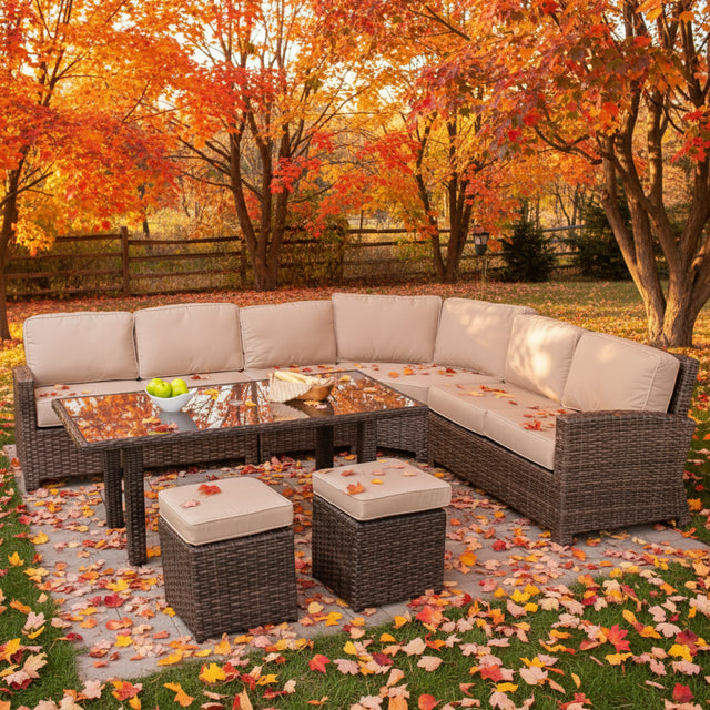 This is a lifestyle image showing this wicker cushioned sectional sofa, coffee table and two ottomans in a nice yard on a sunny, fall day.