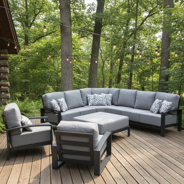 This is a lifestyle image showing the light gray and dark gray colored patio furniture set on a wooden deck on the side of a log cabin. There are hanging lights and trees in the background.