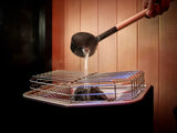 This is a lifestyle image showing someone pouring water on the heat source inside the sauna.