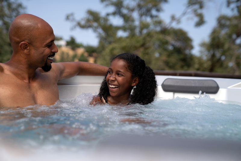 Man and  daughter in a hot tub with trees in the background