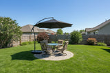 This image shows a grassy backyard with a small, circular stone patio in the center. In the circle there's a patio set with an umbrella over it, offering shade.