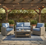 This is a lifestyle image showing this specific patio furniture set on a stone patio underneath a wooden pergola decorated with hanging string lights.