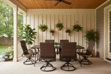 This is a lifestyle image showing this wicker patio dining set on a cover porch. There are hanging plants and potted plants.