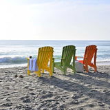 This is a lifestyle image showing three Adirondack chairs facing the ocean on a beach. One chair is Tangerine, one chair is Lime Green and one chair is Yellow.