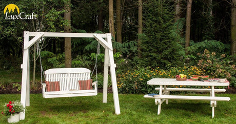 This is a lifestyle image showing the White colored A-frame vinyl swing stand with a matching bench. There's also a matching picnic table with a bunch of fruit and watermelon on top.