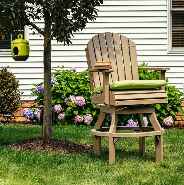 This is a lifestyle image showing the Weatherwood colored swivel Adirondack chair in a grassy garden on the side of a house.