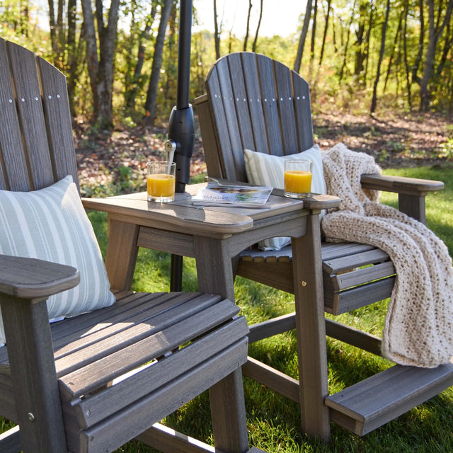 This is a lifestyle image showing two Antique Mahogany colored Adirondack chairs with a matching tete-a-tete table between them.