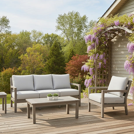 This is a lifestyle image showing this cushioned patio furniture set on a wooden deck next to a wooden trellis decorated with pretty, pink flowers.