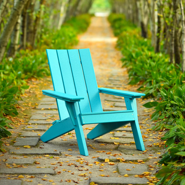 This is a lifestyle image showing the Aruba Blue colored Adirondack chair on a stone walkway surrounded by trees and plants.