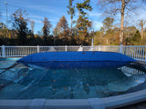 This is a lifestyle image showing the giant Pool Winterizing Pillow under a net cover on a large backyard pool. This image is taken from the side to show how wide the pillow is.
