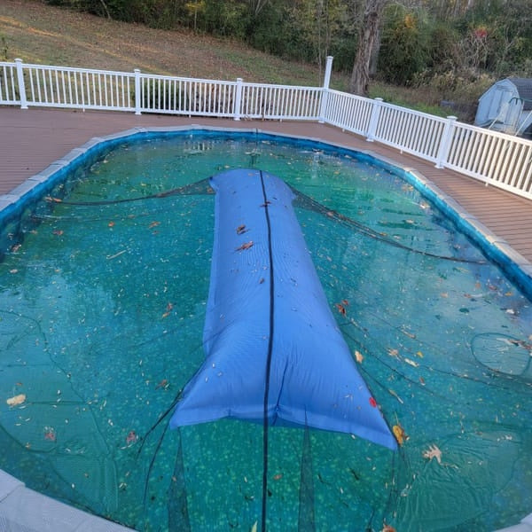 This is a lifestyle image showing the giant Pool Winterizing Pillow under a net cover on a large backyard pool.