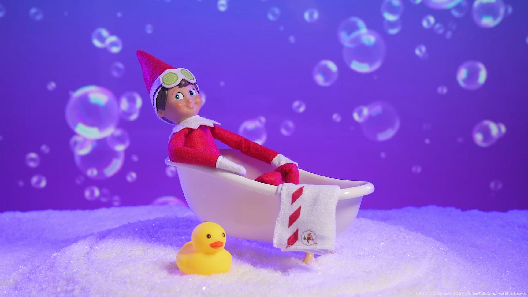 This video showcases the Elf on the Shelf S'elf Care Kit. There's a Scout Elf sitting in the bathtub with bubbles flying around in the background.