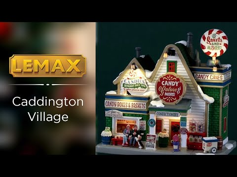 Resin lighted building for a Lemax display. Designed to look like a candy shop. There's a big peppermint sucker on top of the roof that reads "Sweets and More!" Other signs read "Quality Candies devoured since 1948. A sweet place to visit." There's a couple sitting on a red bench in front with a dog. There's also snow throughout
