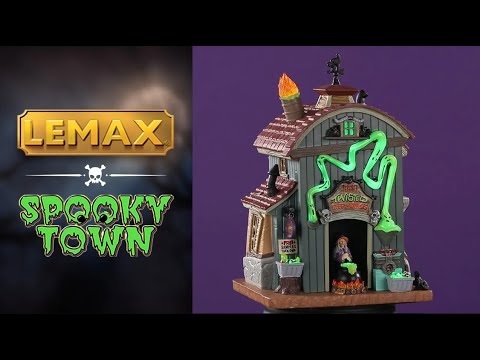 Porcelain lighted building for a Lemax display. Designed to look like a barn that's been turned into a taffy apple shop. There are flames coming out of the chimney and a black cat shaped weather vane. There's a witch in the front door, stirring a boiling cauldron. There's a weird ghost light around the front door that's glowing green.