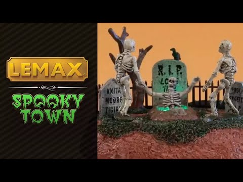Polyresin table accent for a Lemax display. Designed to look like a graveyard with tombstones and a bare tree. There are two skeletons trying to help another skeleton out of a grave. There's a glowing green light coming out of the grave.