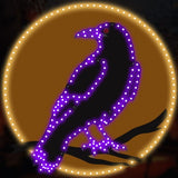 This is a lifestyle image showing what this LED decoration looks like. It's a raven standing on a branch in front of the moon. The moon is lit with warm white lights. The raven is lit with purple lights. The raven's eye is lit with a red light.