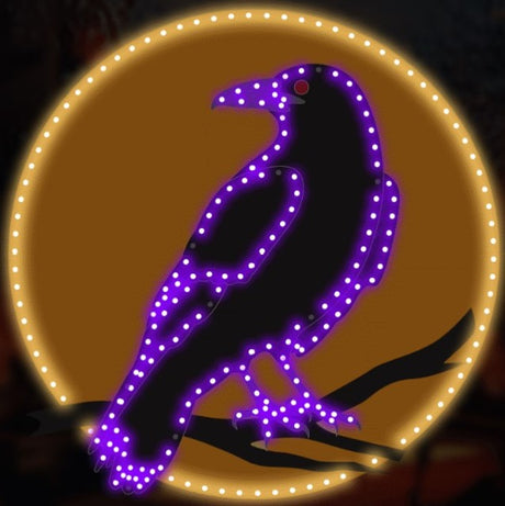 This is a lifestyle image showing what this LED decoration looks like. It's a raven standing on a branch in front of the moon. The moon is lit with warm white lights. The raven is lit with purple lights. The raven's eye is lit with a red light.