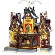 Porcelain lighted building for a Lemax display. Designed to look like a rustic cabin covered in snow and decorated for Christmas. There are angels and pigeons flying above. Santa is waving from a window in the attic. There are reindeer going in a circle around a decorated Christmas tree. There are ornaments for sale on the sidewalk and a nutcracker standing guard at the front door.