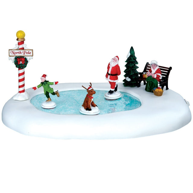 Village accent for a Lemax display. Designed to look like a frozen pond surrounded by snow. There's a child skating on the ice with Santa and a reindeer. Mrs. Claus is sitting on a bench watching.