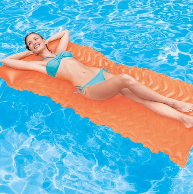 Woman lying on an orange inflatable pool mattress in water.