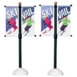Plastic village accessories for a Lemax display. Designed to look like two street poles with banners on them. One side of the banner says "SKI" and features a woman skiing wearing pink winter clothes. The other flag reads "VAIL" and features a person skiing wearing a lime green hoodie, purple pants and a red hat.