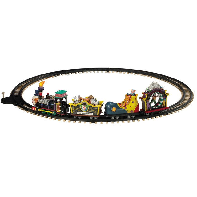 Polyresin train on a set of tracks for a Lemax display. The train cars are all different. The head of the train is the face of a clown. The second one is full of silver and wooden barrels and the side reads "Stitches the Clown: Traveling Mayhem." The third car is shaped like a giant clown shoe. The last one is shaped like a carnival ride where it spins you in a circle.
