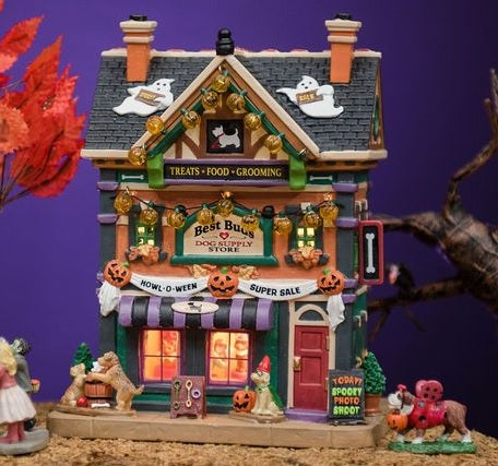 Porcelain lighted building for a Lemax display. Designed to look like a large dog supply store decorated for Halloween. There are ghosts on the roof, pumpkin lights hanging from the roof and a sign with pumpkins that reads "HOWL-O-WEEN SUPER SALE." There are dogs playing in front of the store. There's a sign on the sidewalk that reads "TODAY! SPOOKY PHOTO SHOOT!"