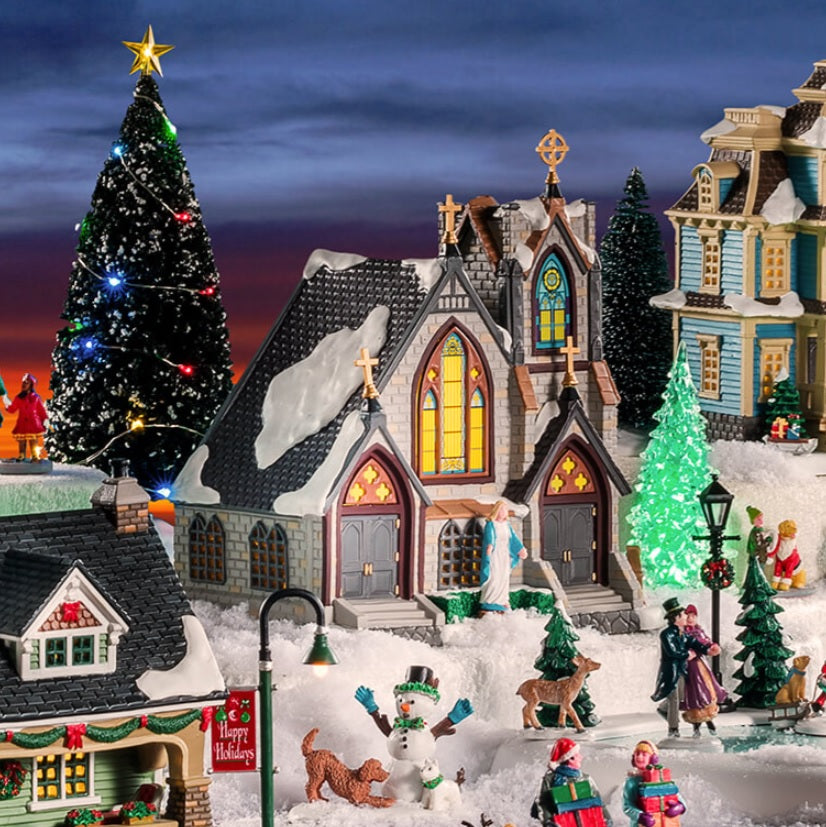 A Lemax tabletop display consisting of a church, light up trees, polyester trees covered in snow, lampposts, a few animals and a couple skating