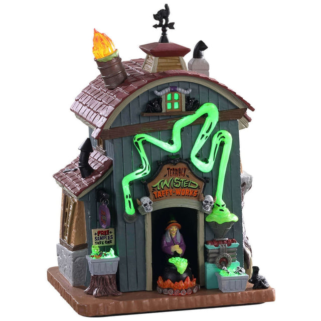 Porcelain lighted building for a Lemax display. Designed to look like a barn that's been turned into a taffy apple shop. There are flames coming out of the chimney and a black cat shaped weather vane. There's a witch in the front door, stirring a boiling cauldron. There's a weird ghost light around the front door that's glowing green.