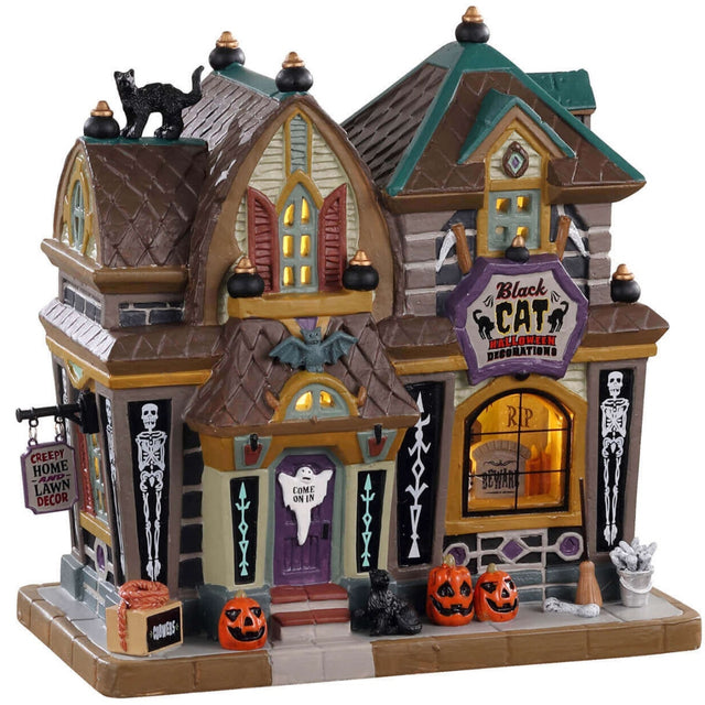 Porcelain lighted building for a Lemax display. Designed to look like a large shop. There's a black cat on the roof and carved pumpkins near the front door. There are skeleton accents and a bat near the front door.
