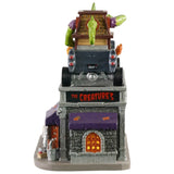 Polyresin and porcelain building for a Lemax Spooky Town display. Designed to look like a mechanic who does custom paint jobs for cars. There's a large green monster on the top, driving a giant car shaped like a house. The sign on the sign of the building reads "THE CREATURE'S."