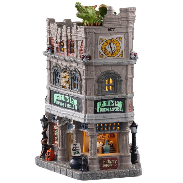 Porcelain lighted building for a Lemax display. Designed to look like a tall, old department store. The signs read "DRAGON'S LAIR POTIONS & SPELLS." There's a green monster on the roof. There are lampposts and a jack-o-lantern accent outside.