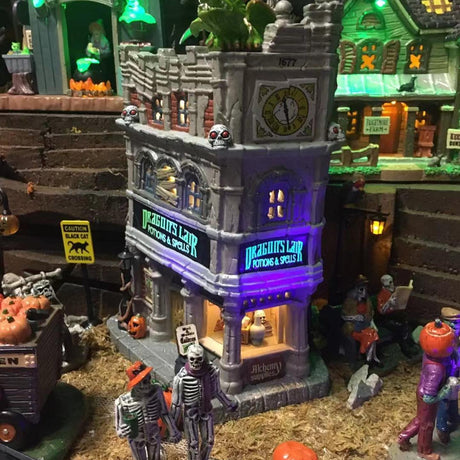 Porcelain lighted building for a Lemax display. Designed to look like a tall, old department store. The signs read "DRAGON'S LAIR POTIONS & SPELLS." There's a green monster on the roof. There are lampposts and a jack-o-lantern accent outside.