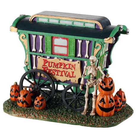 Polyresin village accent for a Lemax display. Designed to look like a green, purple and red cart that reads "PUMPKIN FESTIVAL." There are jack-o-lanterns on the ground and a skeleton standing next to the cart.
