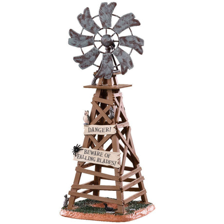 Polyresin table accent for a Lemax display. Designed to look like a wooden windmill with metal blades. There are two signs on it that read "DANGER!" and "BEWARE OF FALLING BLADES!" The danger sign has a small owl sitting on it. The beware sign has a big, black spider on it. There's a little bit of grass and dirt on the ground underneath it. There's a small rat standing at the bottom.